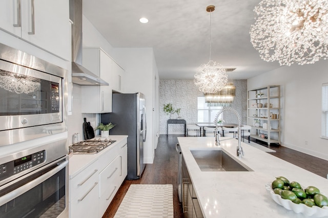 kitchen featuring white cabinets, wall chimney range hood, hanging light fixtures, stainless steel appliances, and a chandelier