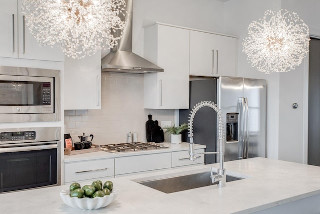 kitchen featuring decorative backsplash, stainless steel appliances, wall chimney range hood, pendant lighting, and a notable chandelier