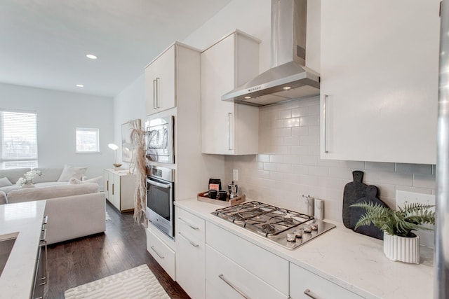 kitchen with white cabinets, wall chimney range hood, dark wood-type flooring, and appliances with stainless steel finishes