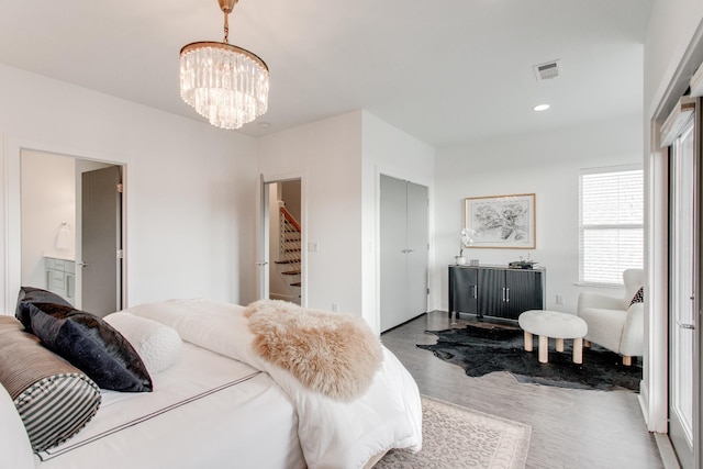 bedroom with wood-type flooring, ensuite bathroom, and an inviting chandelier