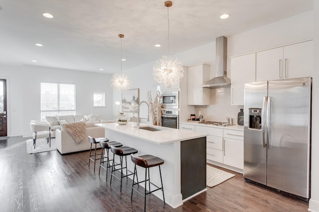 kitchen with pendant lighting, white cabinets, sink, wall chimney exhaust hood, and appliances with stainless steel finishes