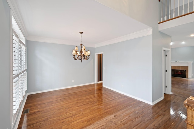 spare room featuring a chandelier, a fireplace, ornamental molding, and hardwood / wood-style flooring