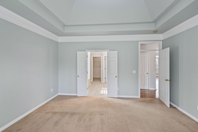 unfurnished bedroom with a raised ceiling, light colored carpet, a walk in closet, and crown molding