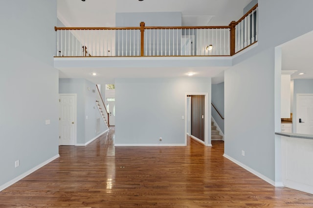 unfurnished living room featuring wood-type flooring and a towering ceiling