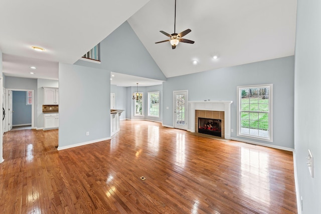 unfurnished living room with a wealth of natural light, a tiled fireplace, high vaulted ceiling, and light hardwood / wood-style flooring