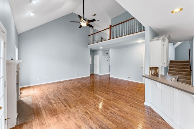 unfurnished living room featuring ceiling fan, high vaulted ceiling, and light wood-type flooring