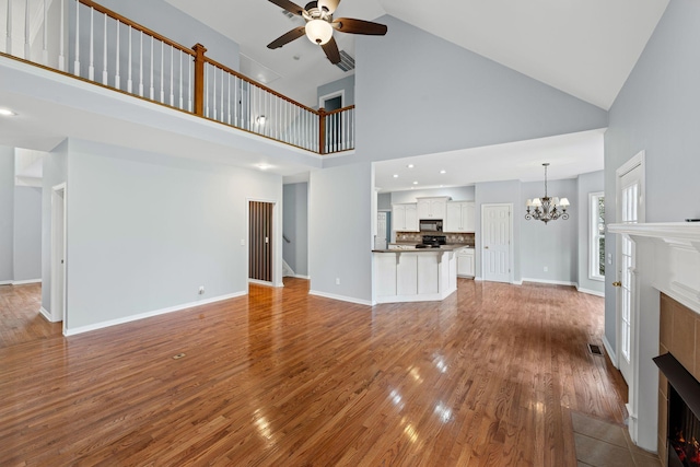 unfurnished living room with hardwood / wood-style floors, high vaulted ceiling, ceiling fan with notable chandelier, and a tile fireplace