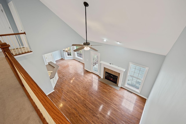 unfurnished living room with a tile fireplace, plenty of natural light, high vaulted ceiling, and wood-type flooring