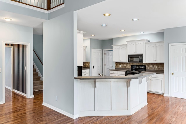 kitchen with white cabinetry, kitchen peninsula, a kitchen bar, black appliances, and hardwood / wood-style flooring