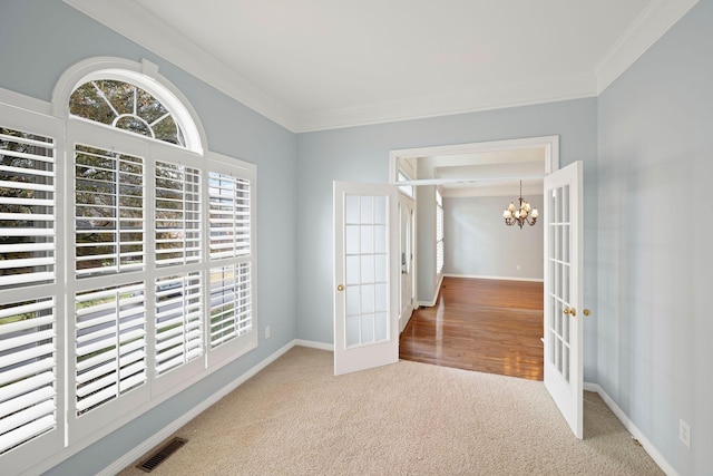 spare room featuring crown molding, french doors, carpet floors, and an inviting chandelier