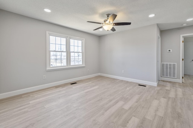 unfurnished room featuring light wood-type flooring, visible vents, a textured ceiling, and baseboards