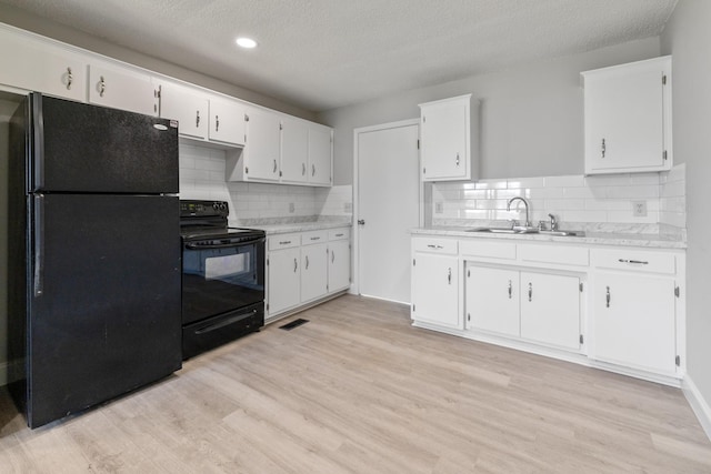 kitchen with a sink, white cabinetry, light countertops, light wood-type flooring, and black appliances