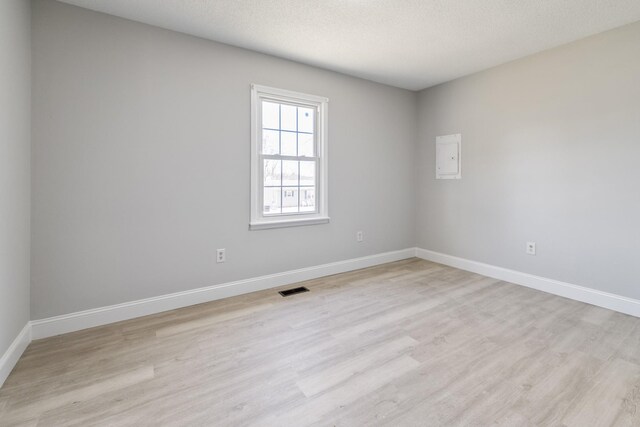 spare room with light wood-type flooring, visible vents, a textured ceiling, and baseboards