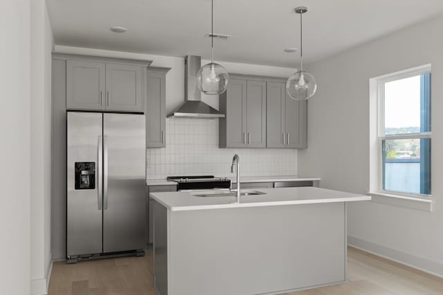 kitchen featuring a center island with sink, sink, wall chimney range hood, and stainless steel refrigerator with ice dispenser