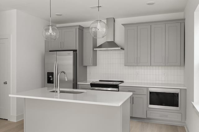 kitchen with an island with sink, pendant lighting, wall chimney range hood, and appliances with stainless steel finishes