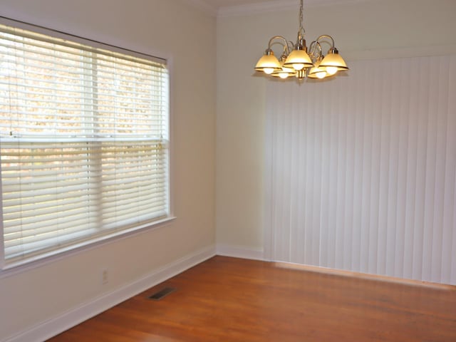 spare room with hardwood / wood-style flooring, ornamental molding, and an inviting chandelier