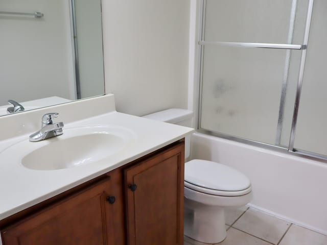 full bathroom with tile patterned flooring, vanity, bath / shower combo with glass door, and toilet