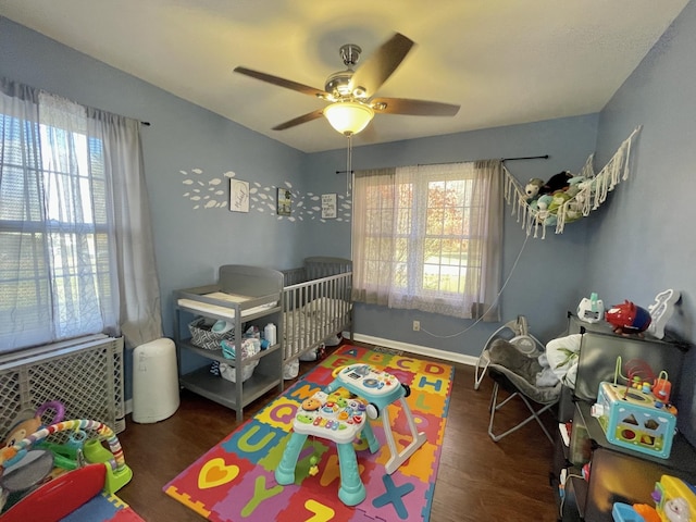 bedroom featuring ceiling fan, dark hardwood / wood-style flooring, a crib, and multiple windows