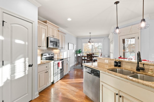 kitchen featuring pendant lighting, sink, light wood-type flooring, appliances with stainless steel finishes, and cream cabinets