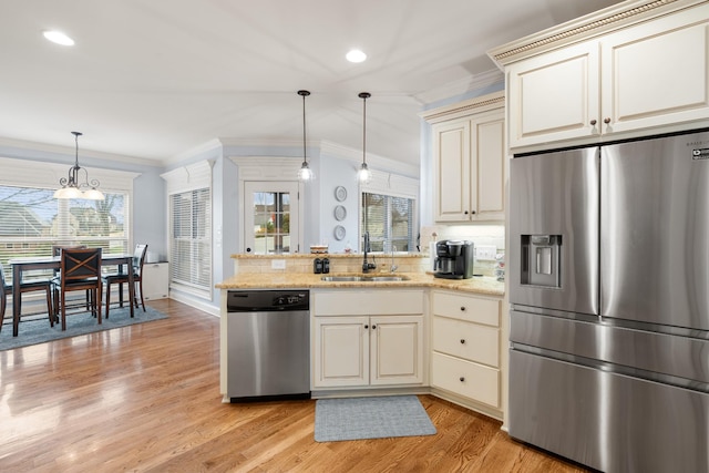 kitchen with decorative light fixtures, stainless steel appliances, sink, ornamental molding, and cream cabinetry