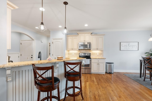 kitchen featuring decorative backsplash, light hardwood / wood-style flooring, hanging light fixtures, stainless steel appliances, and ornamental molding