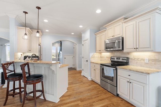 kitchen featuring light hardwood / wood-style floors, appliances with stainless steel finishes, decorative backsplash, hanging light fixtures, and light stone countertops