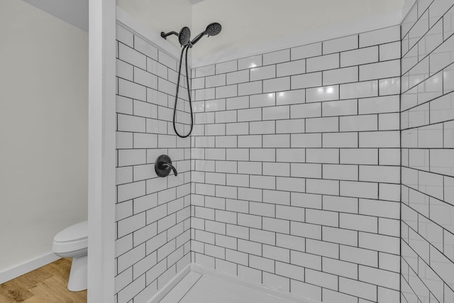 bathroom featuring a tile shower, toilet, and hardwood / wood-style flooring