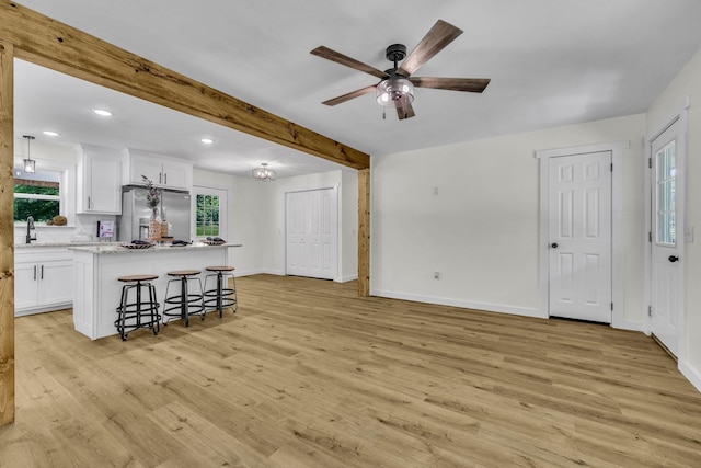 kitchen with stainless steel refrigerator with ice dispenser, a kitchen island, light hardwood / wood-style floors, white cabinetry, and a breakfast bar area