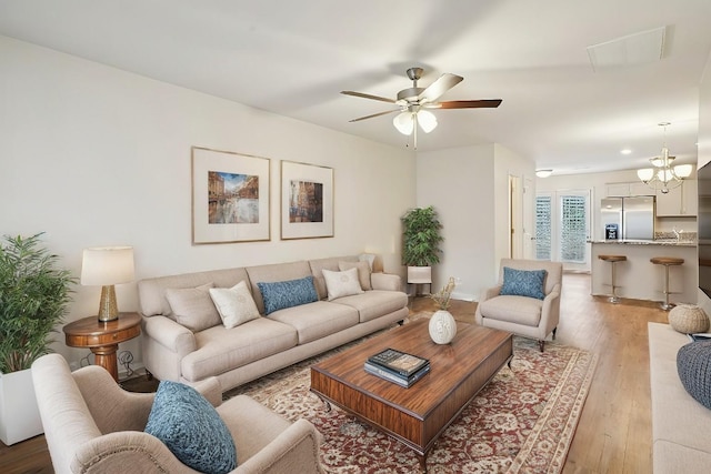 living room featuring ceiling fan with notable chandelier and light wood-type flooring