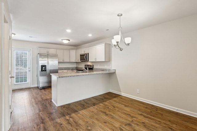 kitchen featuring kitchen peninsula, appliances with stainless steel finishes, light stone countertops, pendant lighting, and white cabinets