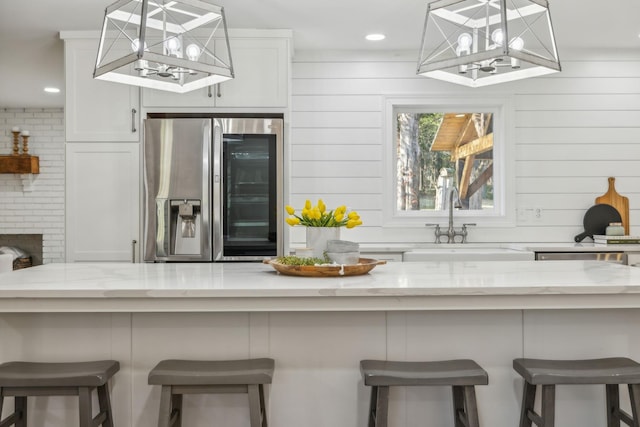 kitchen featuring white cabinets, stainless steel fridge with ice dispenser, hanging light fixtures, and a kitchen breakfast bar