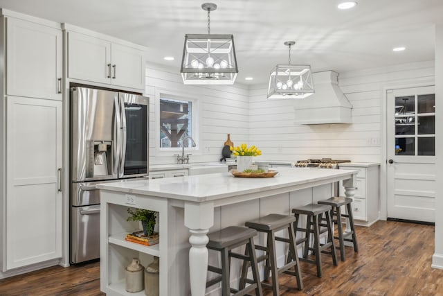 kitchen with stainless steel refrigerator with ice dispenser, premium range hood, dark wood-type flooring, white cabinetry, and a kitchen island