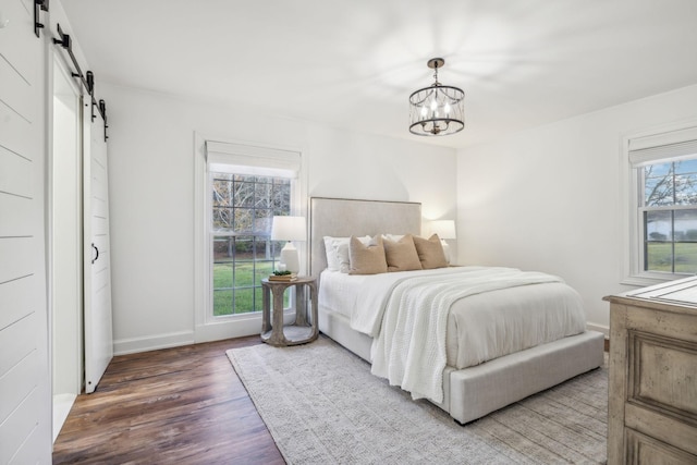 bedroom featuring a chandelier, a barn door, dark hardwood / wood-style floors, and multiple windows