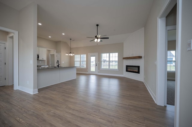 unfurnished living room featuring sink, a large fireplace, ceiling fan with notable chandelier, and hardwood / wood-style flooring