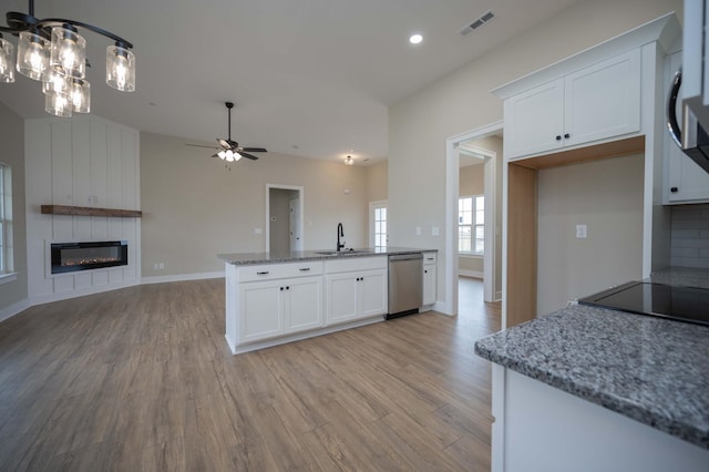 kitchen featuring sink, light stone counters, stainless steel dishwasher, a fireplace, and white cabinets