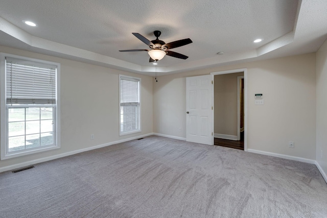 unfurnished room featuring carpet, a tray ceiling, ceiling fan, and a healthy amount of sunlight