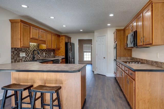 kitchen with a breakfast bar, a textured ceiling, sink, black appliances, and dark hardwood / wood-style floors