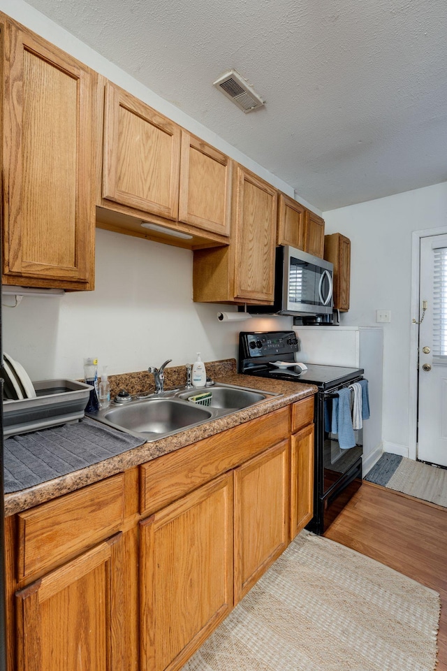 kitchen with electric range, sink, light hardwood / wood-style floors, and a textured ceiling