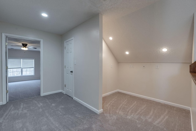 additional living space featuring dark colored carpet, ceiling fan, a textured ceiling, and vaulted ceiling