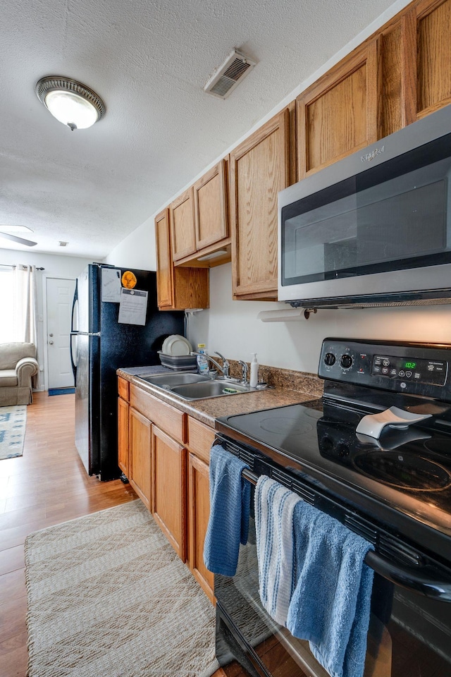 kitchen with sink, black appliances, a textured ceiling, and light hardwood / wood-style floors