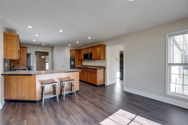 kitchen featuring dark wood-type flooring, black appliances, sink, kitchen peninsula, and a breakfast bar area