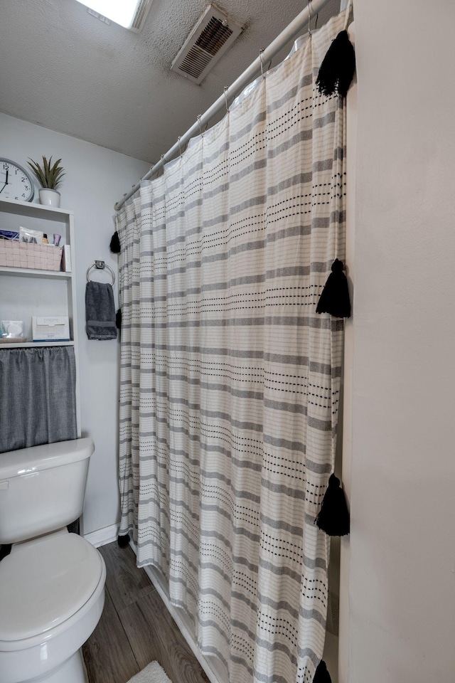 bathroom featuring hardwood / wood-style flooring, curtained shower, toilet, and a textured ceiling