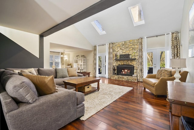 living room featuring dark wood-type flooring, a stone fireplace, a skylight, a notable chandelier, and beam ceiling