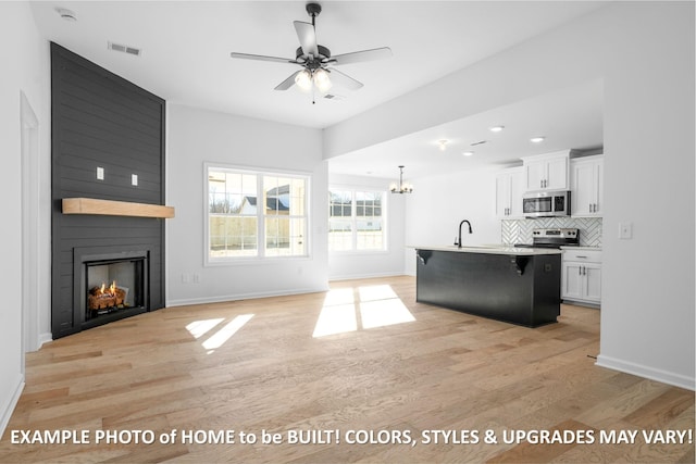 kitchen featuring white cabinetry, open floor plan, light countertops, appliances with stainless steel finishes, and an island with sink