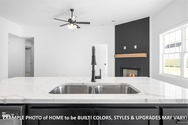 kitchen featuring a fireplace, a ceiling fan, a sink, light stone countertops, and dishwasher