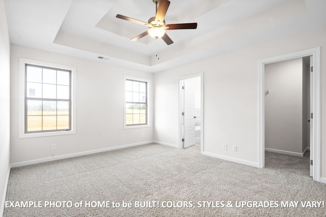 unfurnished bedroom with baseboards, a tray ceiling, a walk in closet, and light colored carpet