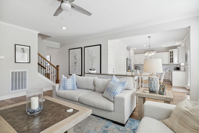 living room featuring crown molding, light hardwood / wood-style floors, and ceiling fan with notable chandelier