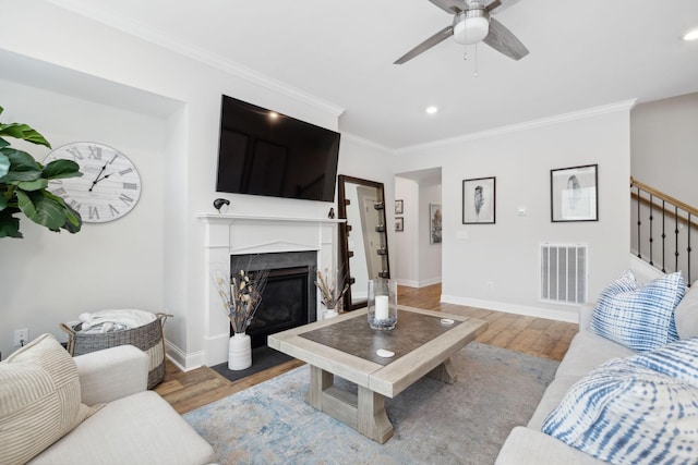 living room featuring a premium fireplace, crown molding, ceiling fan, and hardwood / wood-style flooring