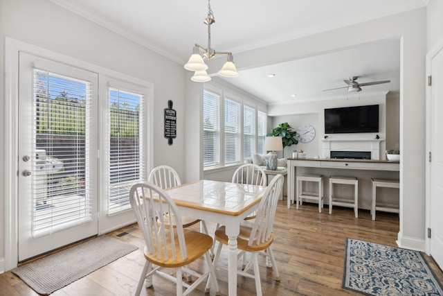 dining area featuring wood-type flooring, ceiling fan with notable chandelier, and ornamental molding