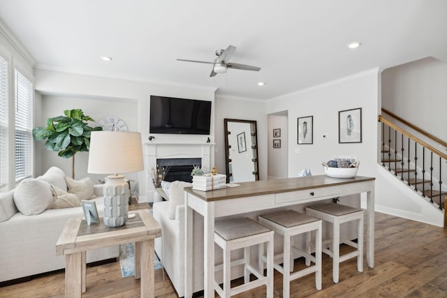 living room featuring wood-type flooring, ceiling fan, and crown molding